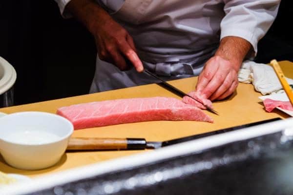 A chef skillfully prepares fresh raw fatty tuna for his customers